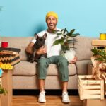 Image of positive fashionable guy rents new flat, lives together with favourite dog, sits on couch,