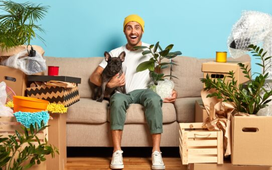 Image of positive fashionable guy rents new flat, lives together with favourite dog, sits on couch,